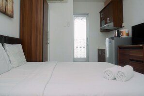 Une chambre d’hôtel avec un lit, une petite kitchenette et une vue sur l’extérieur, visible à travers une porte.