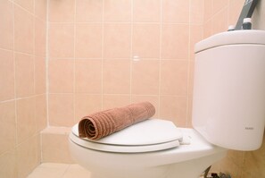 Des toilettes avec une serviette enroulée posée sur le siège et un porte-rouleau de papier toilette fixé sur le réservoir.