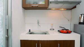 Una cocina con un lavamanos de acero inoxidable, una estufa eléctrica roja, armarios de madera y una encimera blanca.