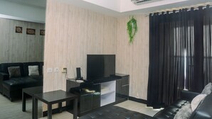 Un salon moderne avec un canapé en cuir noir, une table basse noire, un téléviseur à écran plat posé sur un meuble noir et un mur en bois orné d’une plante suspendue.