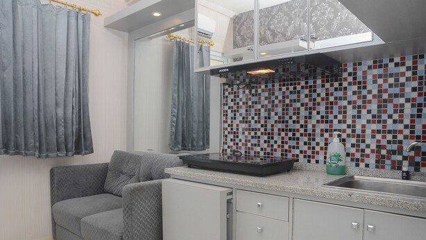 A modern kitchen with a grey sofa, a tiled backsplash, and a built-in oven. - Comfortable and Clean 2BR Green Pramuka Apartment (Jakarta)