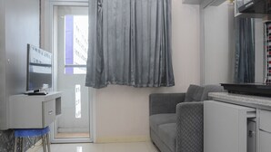 A compact living space with a kitchenette, a grey sofa, and a small desk with a computer. - Comfortable and Clean 2BR Green Pramuka Apartment (Jakarta)