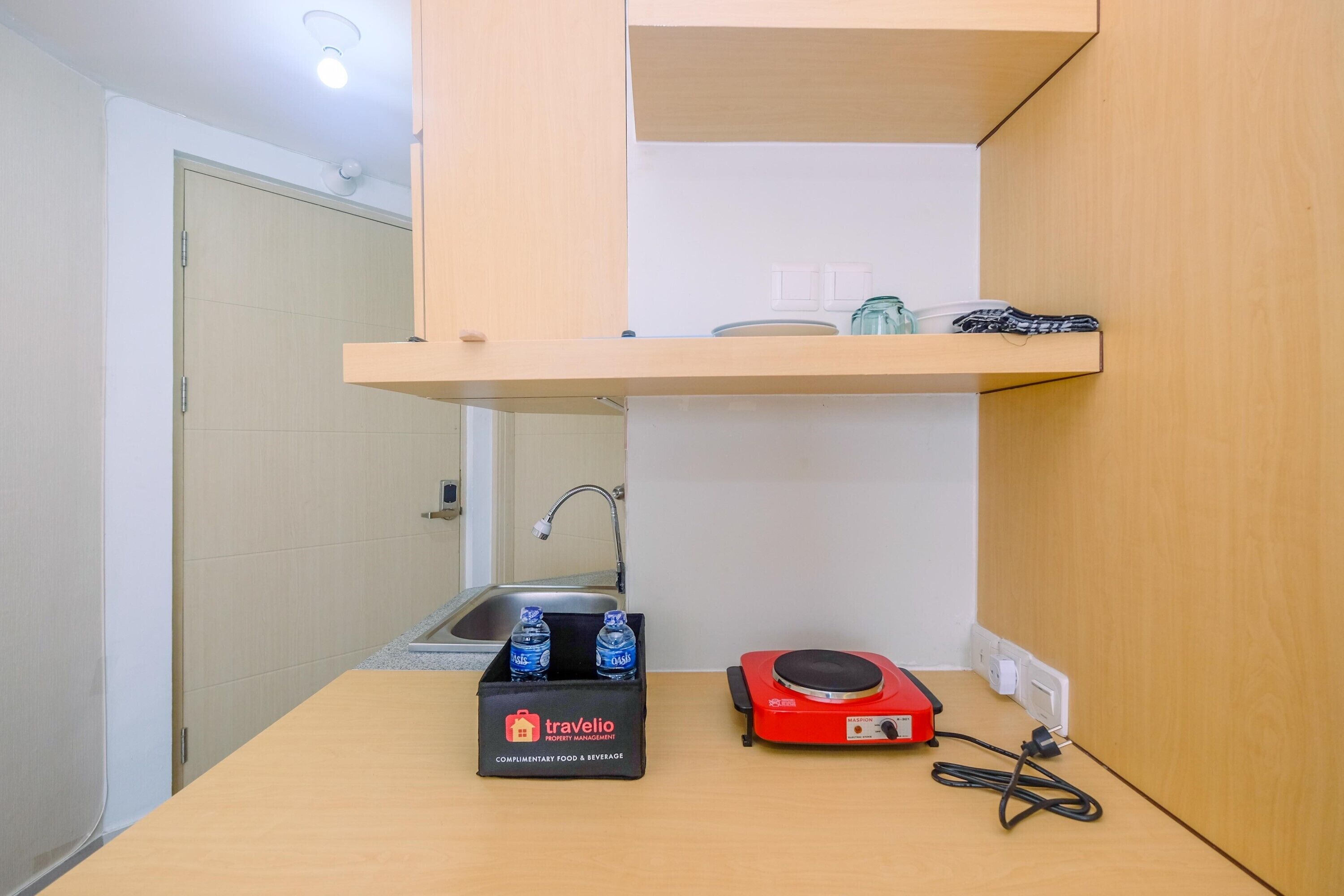 A compact kitchenette with a sink, a small countertop, a travelio branded box, and a red portable heater.