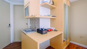 A compact kitchen with wooden cabinets, a microwave, a kettle, and a coffee maker on a shelf. - Relaxing and Stylish Studio at Amethyst Tower Apartment (Jakarta)
