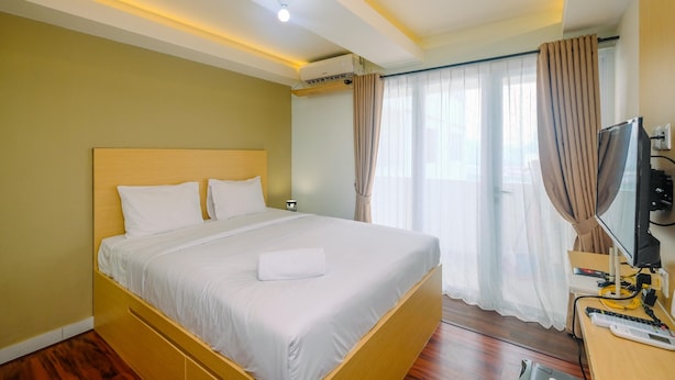 A hotel room with a large bed, a desk with a computer, and a TV. - Relaxing and Stylish Studio at Amethyst Tower Apartment (Jakarta)