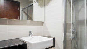 Un baño con un lavamanos blanco, un espejo y una cabina de ducha con paredes de vidrio.