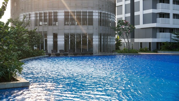 Un edificio moderno con fachada curva, piscina y vegetación circundante.