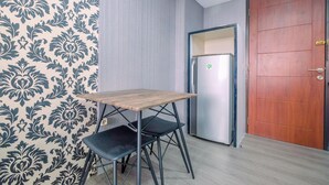 A room with a wooden table and two black chairs, a refrigerator, and a wooden door. - Comfy and New Furnished @ 2BR Kebagusan City Apartment (Jakarta)
