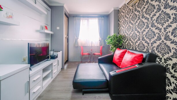 A modern living room with a flat-screen TV, a black leather sofa with red cushions, a dining table with chairs, and a potted plant. - Comfy and New Furnished @ 2BR Kebagusan City Apartment (Jakarta)