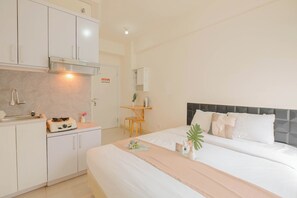Quarto de hotel moderno com cama bem arrumada, pequeno espaço de cozinha e escrivaninha com cadeira.