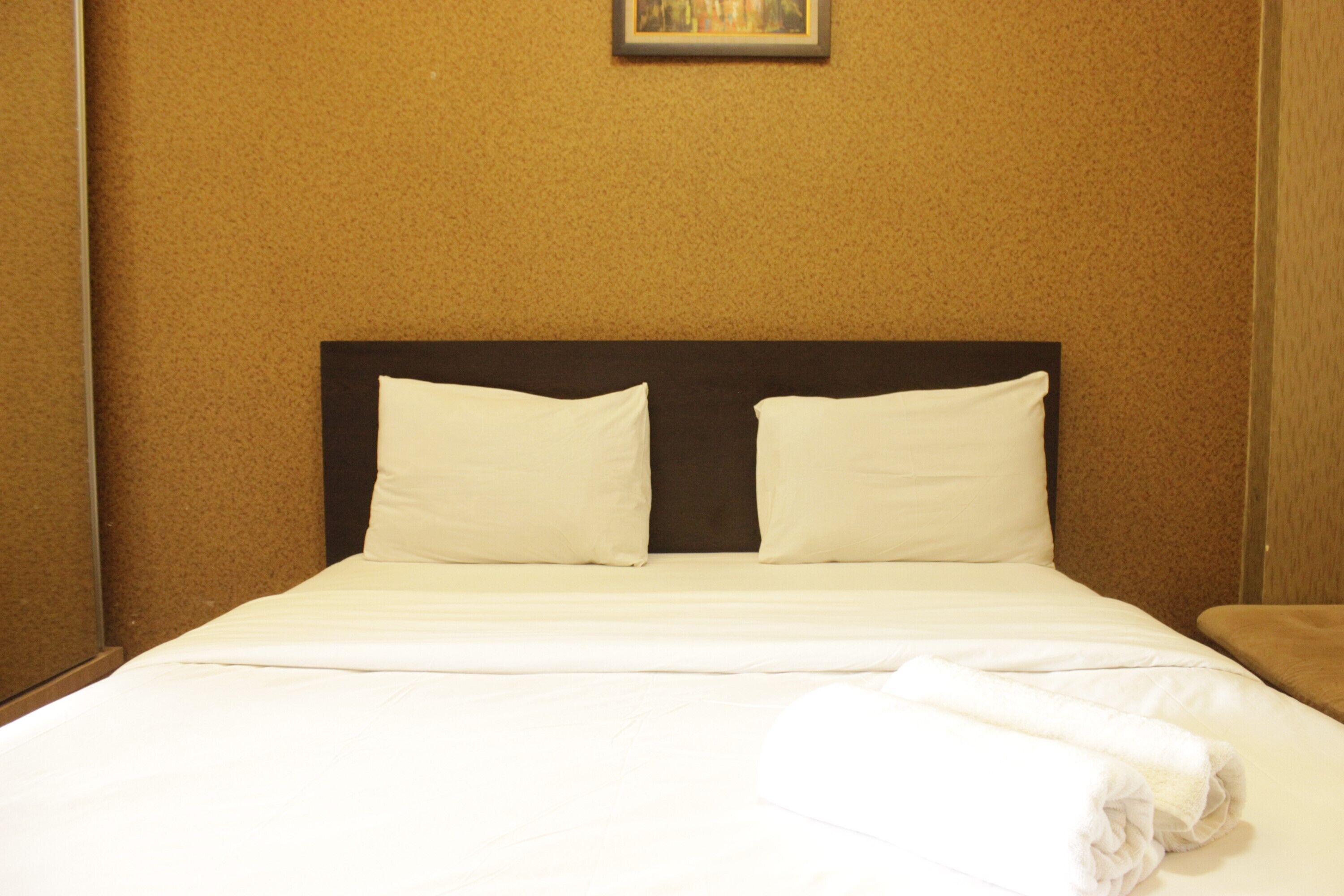 A neatly made bed with white linens and pillows, a dark headboard, and a folded white towel on the side.