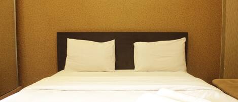 A neatly made bed with white linens and pillows, a dark headboard, and a folded white towel on the side.