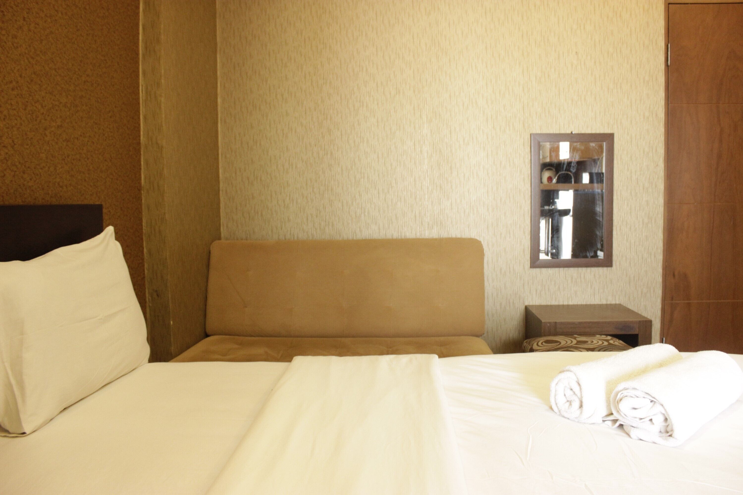 A hotel room with a bed, a nightstand, a mirror, and a wooden door.