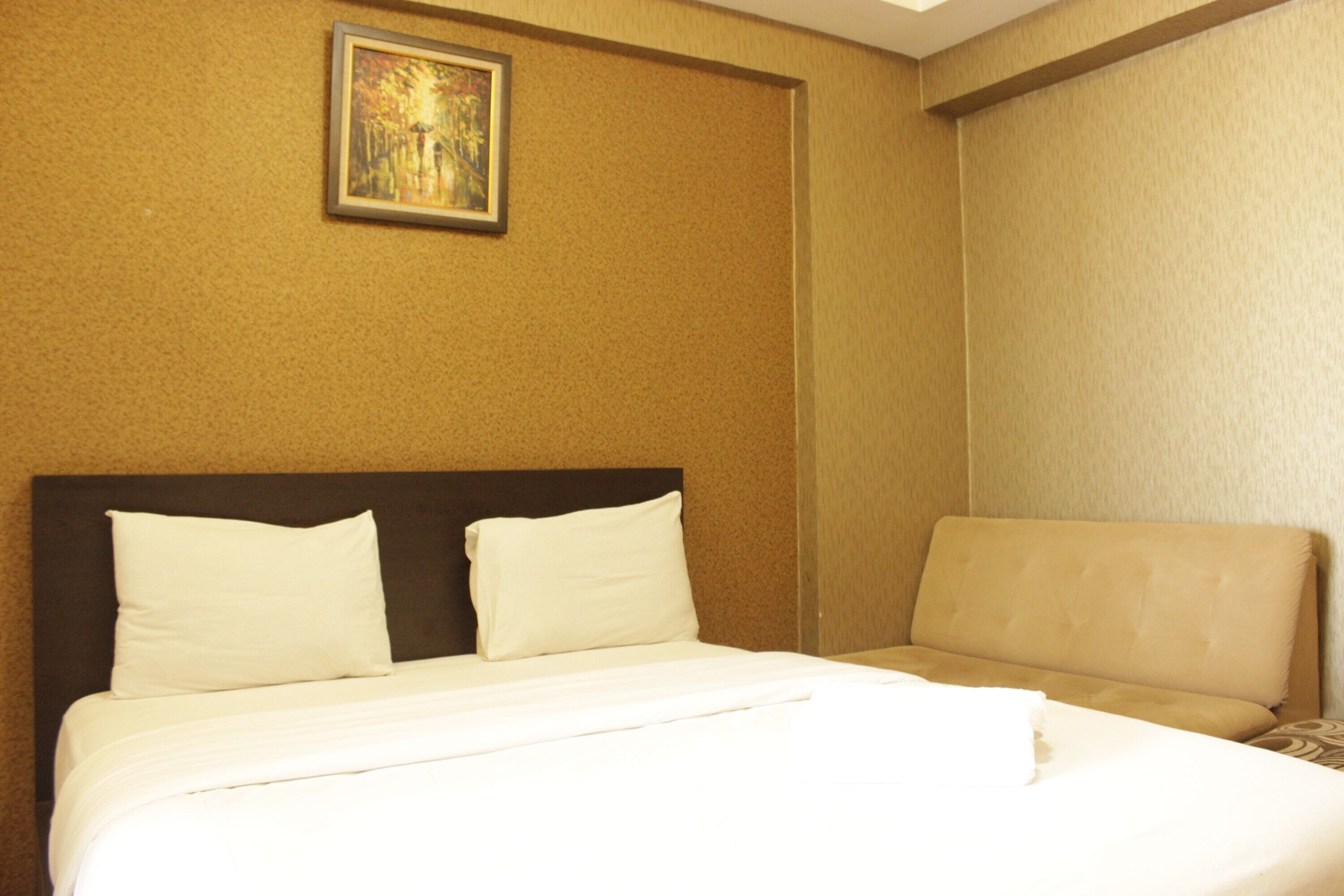 A hotel room with a large bed, a headboard, a wall-mounted painting, and a seating area with a cushioned bench.
