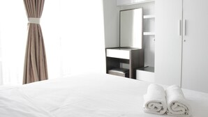A hotel room with a neatly made bed, a large mirror, a vanity with a mirror, and a wardrobe. - Pleasant 1BR Apartment with Sofa Bed at Dago Suites (Bandung)