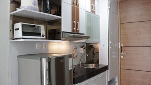 A compact kitchen with a stainless steel refrigerator, a built-in oven, and a sink. - Pleasant 1BR Apartment with Sofa Bed at Dago Suites (Bandung)