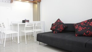 A modern living area with a dark sofa, white chairs, and a small table. - Pleasant 1BR Apartment with Sofa Bed at Dago Suites (Bandung)