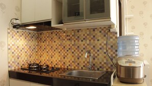 A kitchen with a tiled backsplash, a stove, a sink, and a water dispenser. - Comfy & Strategic 2BR Gateway Pasteur Apartment near Pasteur Exit Toll (Cimahi)