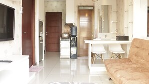A modern living room with a sofa, a TV, and a kitchen area with a water dispenser and a refrigerator. - Comfy & Strategic 2BR Gateway Pasteur Apartment near Pasteur Exit Toll (Cimahi)