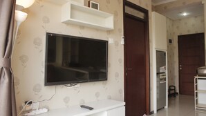 A living room with a flat-screen TV mounted on the wall, a white entertainment unit below, and a wooden door to the right. - Comfy & Strategic 2BR Gateway Pasteur Apartment near Pasteur Exit Toll (Cimahi)
