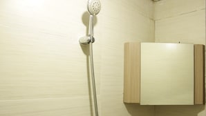 A shower with a handheld showerhead mounted on a wall, a wooden cabinet below it, and tiled walls.