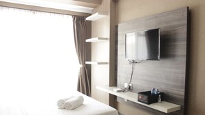 A modern hotel room with a large bed, a mounted TV, and a shelf with toiletries.