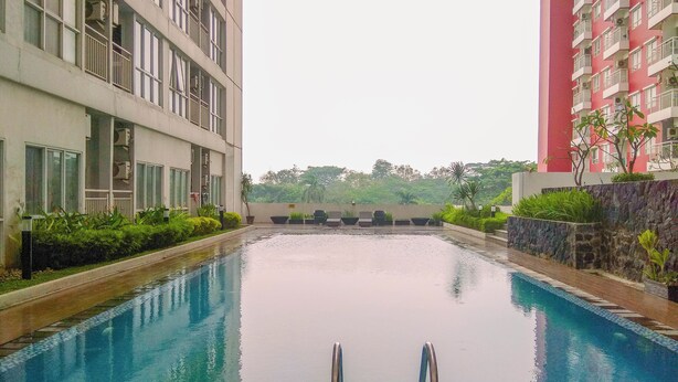 A swimming pool with a clear view of the surrounding buildings, a stone wall, and some greenery. - Modern Studio Apartment at Taman Melati Margonda near Universitas Indonesia (Depok)
