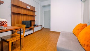 A modern living room with a wooden TV stand, a sofa with orange cushions, and a wooden dining table with chairs. - Modern Furnished @ 1BR Margonda Residence 1 Apartment (Depok)