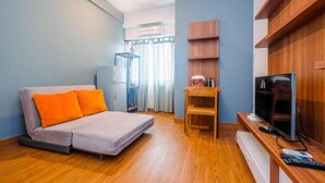 A compact living space with a sofa, a television, a wooden shelf, and a window with curtains. - Modern Furnished @ 1BR Margonda Residence 1 Apartment (Depok)