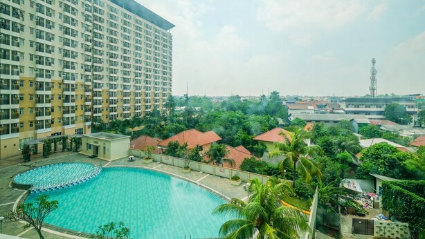 A large swimming pool surrounded by greenery and residential buildings. - Modern Furnished @ 1BR Margonda Residence 1 Apartment (Depok)