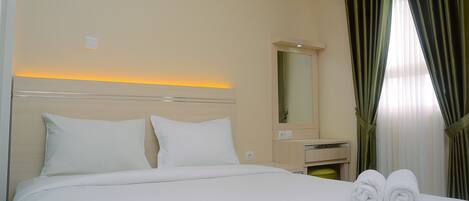 A neatly made bed with white linens, a bedside table with a mirror, and two rolled towels on the bed.