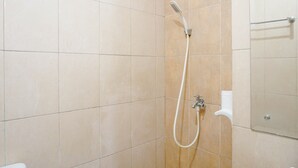 Une salle de bain carrelée de carreaux beiges, une douche avec un pommeau de douche amovible et un miroir.
