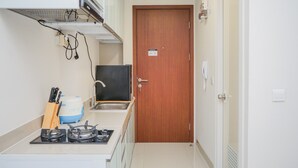 A compact kitchen with a gas stove, sink, and a microwave. There is a wooden cutting board and a knife block on the counter. A wooden door with a sign is visible in the background. - Elegant Studio Parkland Avenue Apartment (South Tangerang)