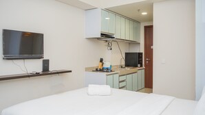 A hotel room with a bed, a TV mounted on the wall, a kitchenette with a microwave, and a small sink. - Elegant Studio Parkland Avenue Apartment (South Tangerang)