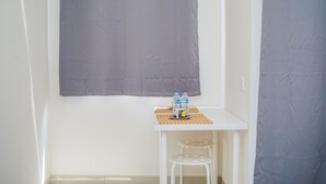 A small room with a white table, two white chairs, a window with a grey curtain, and a bottle of water on the table. - Elegant Studio Parkland Avenue Apartment (South Tangerang)