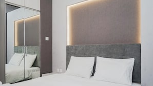 A modern bedroom with a large bed, a grey headboard, and a mirror reflecting the room. - Clean and Tidy Studio Room at Tree Park Apartment (South Tangerang)