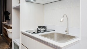 A modern kitchen with a built-in gas stove, a sink, and a faucet. - Clean and Tidy Studio Room at Tree Park Apartment (South Tangerang)