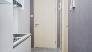 A narrow hallway with a door, a kitchen area with a sink, and a thermostat on the wall. - Clean and Tidy Studio Room at Tree Park Apartment (South Tangerang)