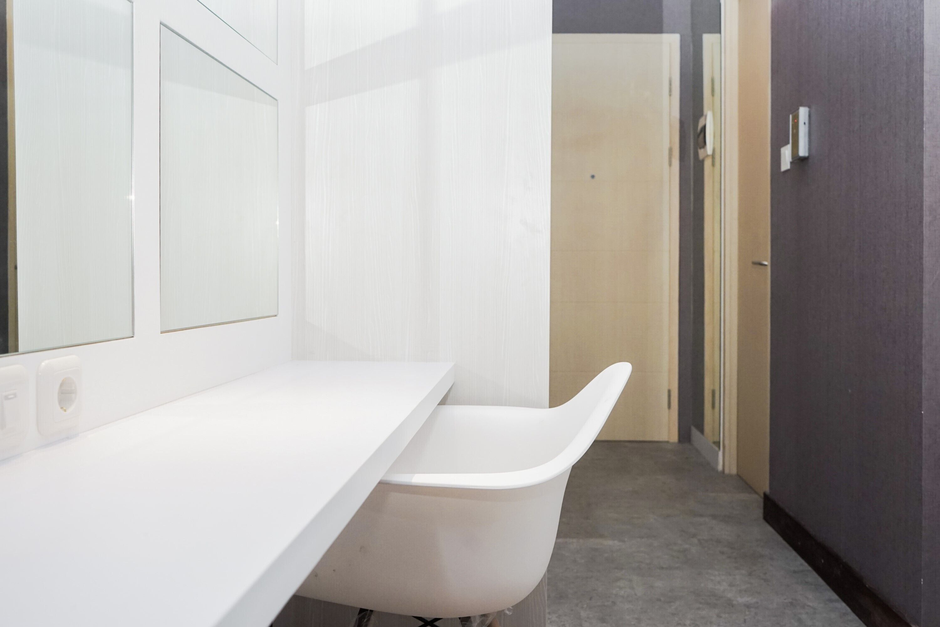 Un baño moderno con encimera blanca, una bañera blanca y una puerta que da a otra habitación.