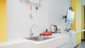 A modern kitchen with a white countertop, a stainless steel sink, a red electric kettle, and a wall-mounted television. - Studio Apartment at Tree Park Apartment (South Tangerang)
