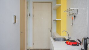 A small kitchenette with a sink, a red electric kettle, and a yellow accent wall. - Studio Apartment at Tree Park Apartment (South Tangerang)