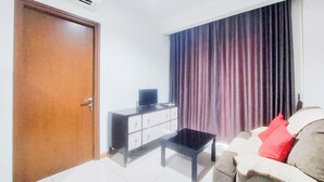 Ein Wohnzimmer mit Holztür, einem Fernseher auf einem Schrank, einer Couch mit Kissen und einem großen Fenster mit Vorhängen.