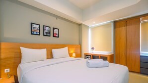 A hotel room with a large bed, wooden headboard, bedside tables with lamps, a small table with a glass, and a wooden wardrobe. - Luxury 1BR Apartment with Golf View at Mustika Golf Residence (Cikarang)
