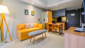 A modern living room with a sofa, a coffee table, a dining area with a table and chairs, and a kitchen in the background. - Luxury 1BR Apartment with Golf View at Mustika Golf Residence (Cikarang)