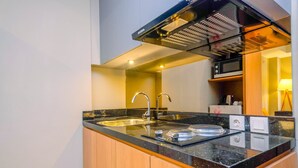 A modern kitchen with a black countertop, stainless steel sink, and a built-in microwave. - Luxury 1BR Apartment with Golf View at Mustika Golf Residence (Cikarang)