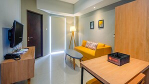 A modern hotel room with a wooden desk, a television, a sofa, and a lamp. - Luxury 1BR Apartment with Golf View at Mustika Golf Residence (Cikarang)