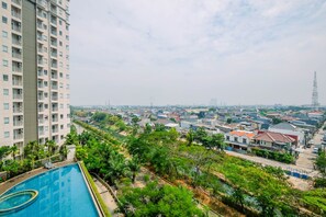Un edificio alto con piscina, rodeado de vegetación y otros edificios residenciales.