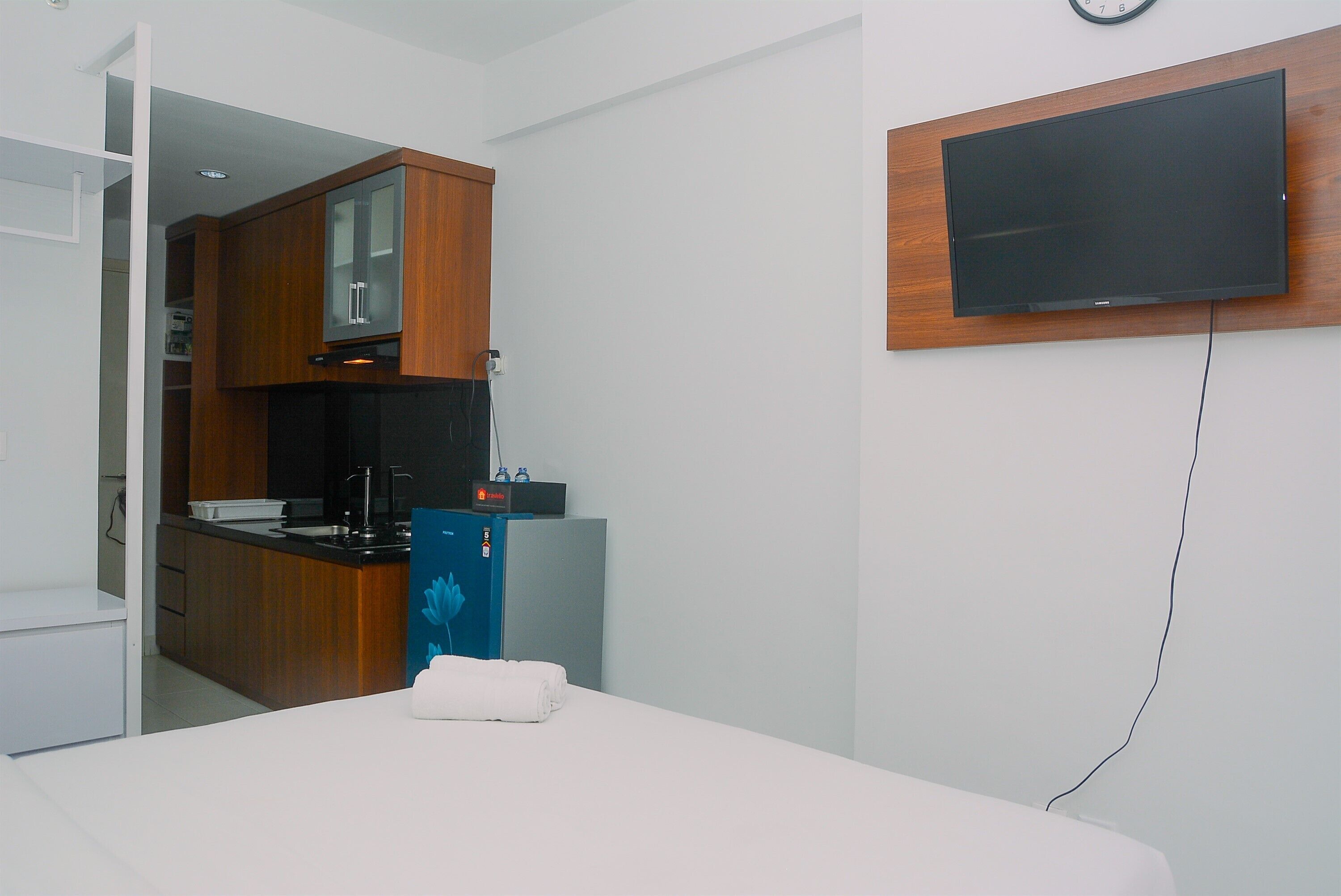 Ein modernes Hotelzimmer mit einer Küchenzeile, einem an der Wand befestigten Flachbildfernseher und einem ordentlich bezogenen Bett.