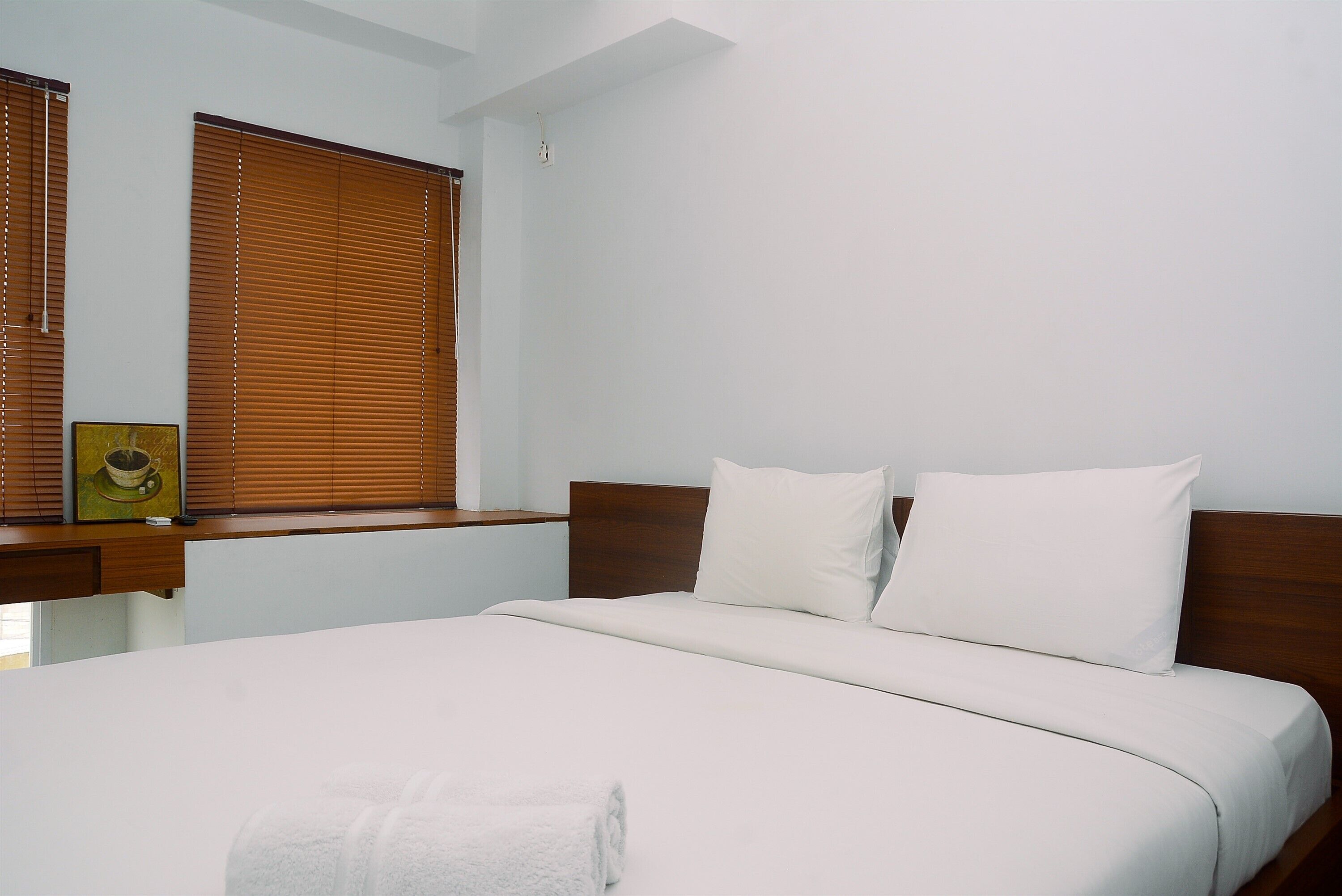Ein ordentlich gemachtes Bett mit weißen Leinen und Kissen, ein Holz-Kopfstück und ein Nachttisch mit einem gerahmten Bild.