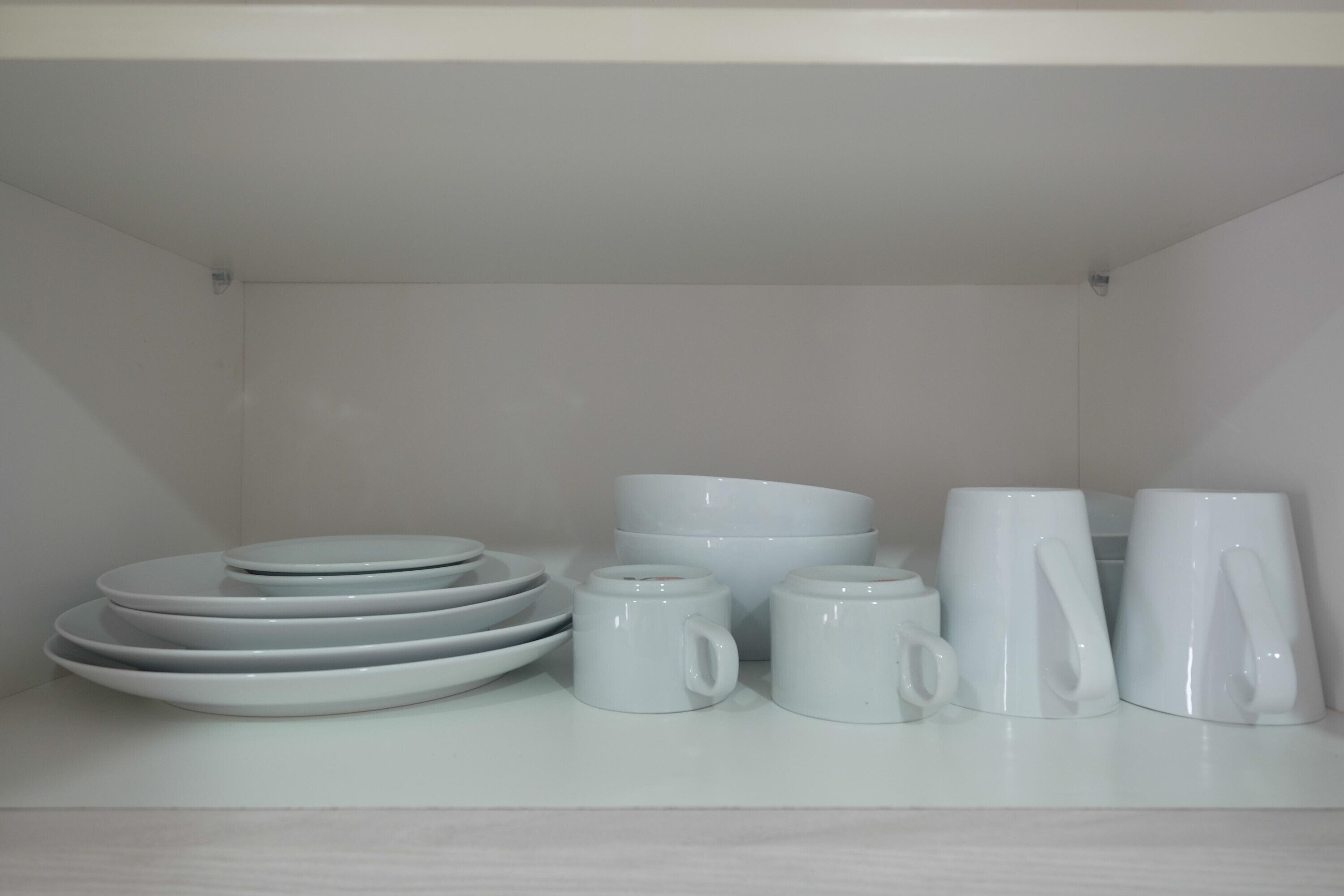 Une étagère blanche sur laquelle sont empilées des assiettes, des bols et des tasses.